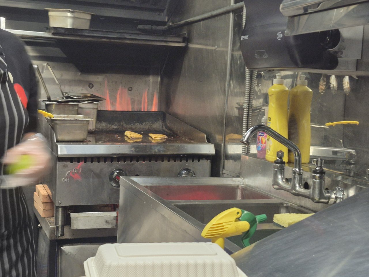 Actual kitchen showing the griddle cooking surface, hood and stainless-steel sinks